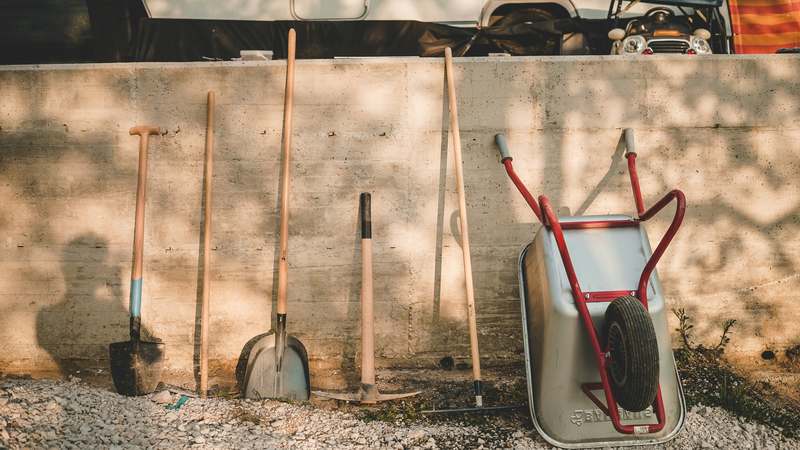 Close-up of a high-quality stainless steel garden shovel in rich soil with fresh mulch and green foliage in soft natural light